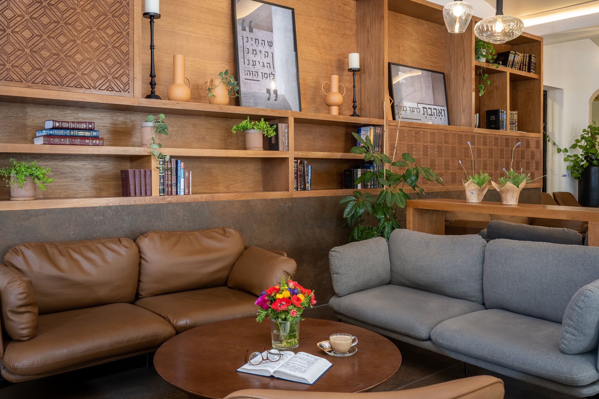 A modern living room with leather sofas, a coffee table with a book and flowers, and a bookshelf with books and decorative items.
