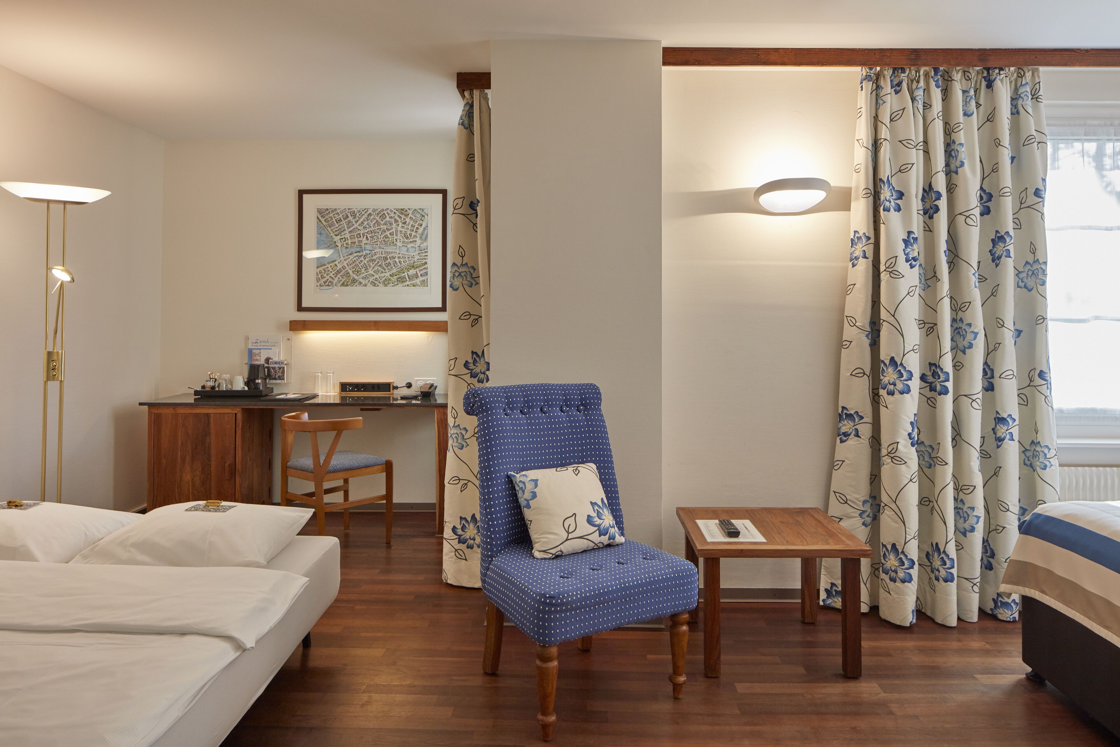 Habitación de hotel con cama, escritorio, silla, mesita y ventana con cortinas.