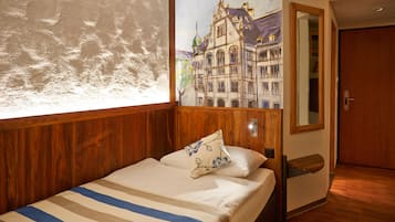 A hotel room with a wooden headboard, a bed with striped bedding, a large window, and a wall mural of a building.