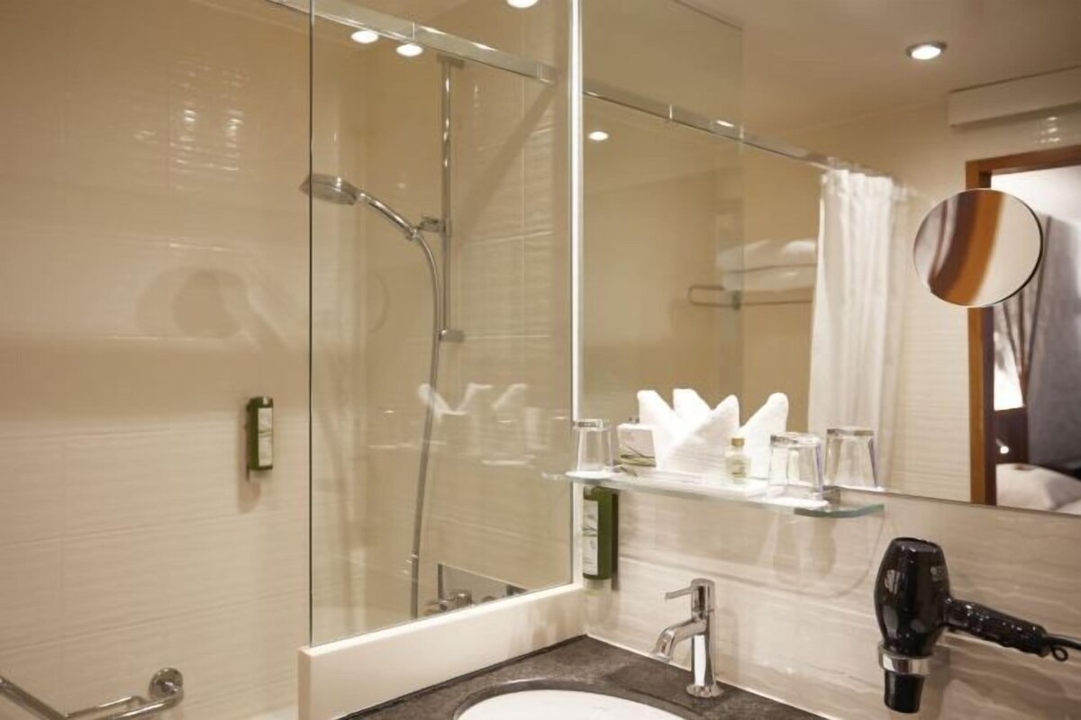 A modern bathroom with a glass shower enclosure, a sink with a mirror, and a hairdryer on the counter.