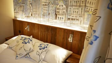 A bed with floral pillows, a wooden headboard, and a cityscape mural above it.