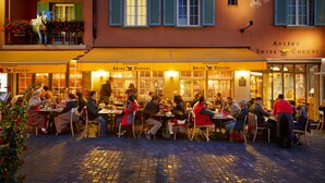 En restaurant kaldet 'Swiss Chuchi' med udendørs siddepladser på en brostensbelagt gade.