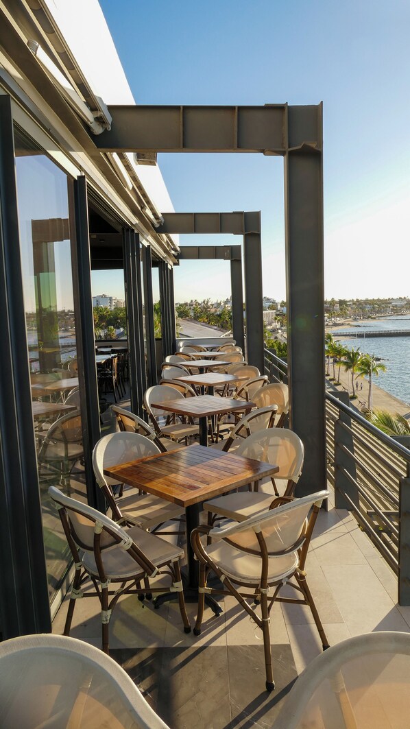 Un espace extérieur aménagé pour les repas, avec des tables et des chaises, offrant une vue sur le bord de l’eau.