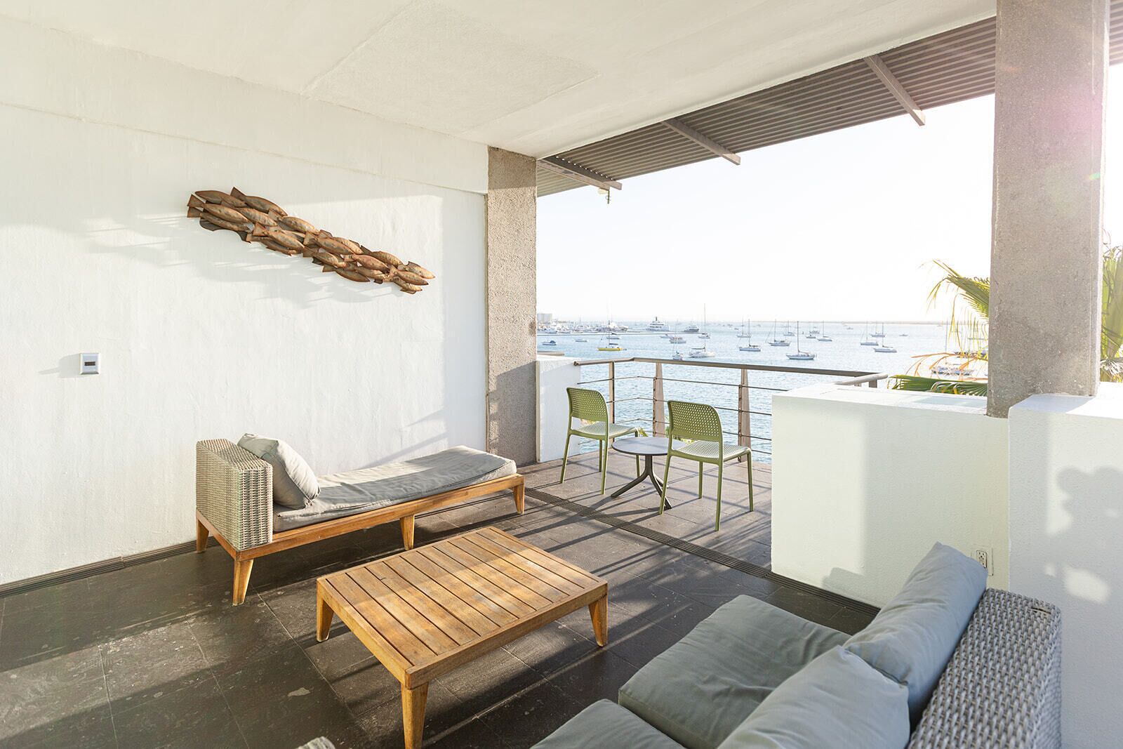 A balcony with a wooden bench, a sofa, and two chairs, overlooking a marina with boats.