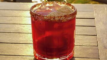 Et glas rød drik med saltkant på et træbord ved et gelænder med udsigt til vand og grønt.