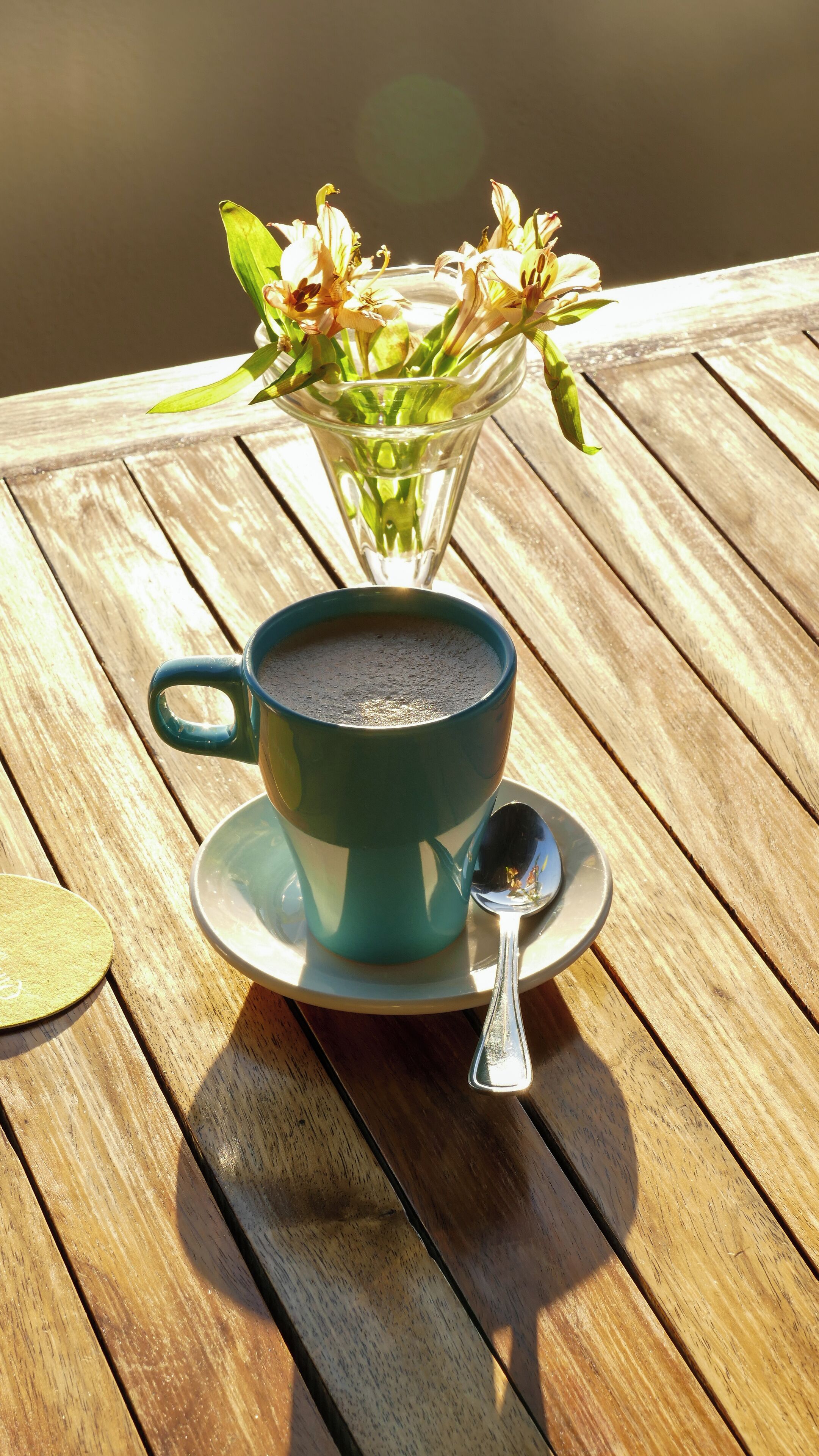 Une tasse de café turquoise posée sur une table en bois, avec une cuillère et une soucoupe à côté.
