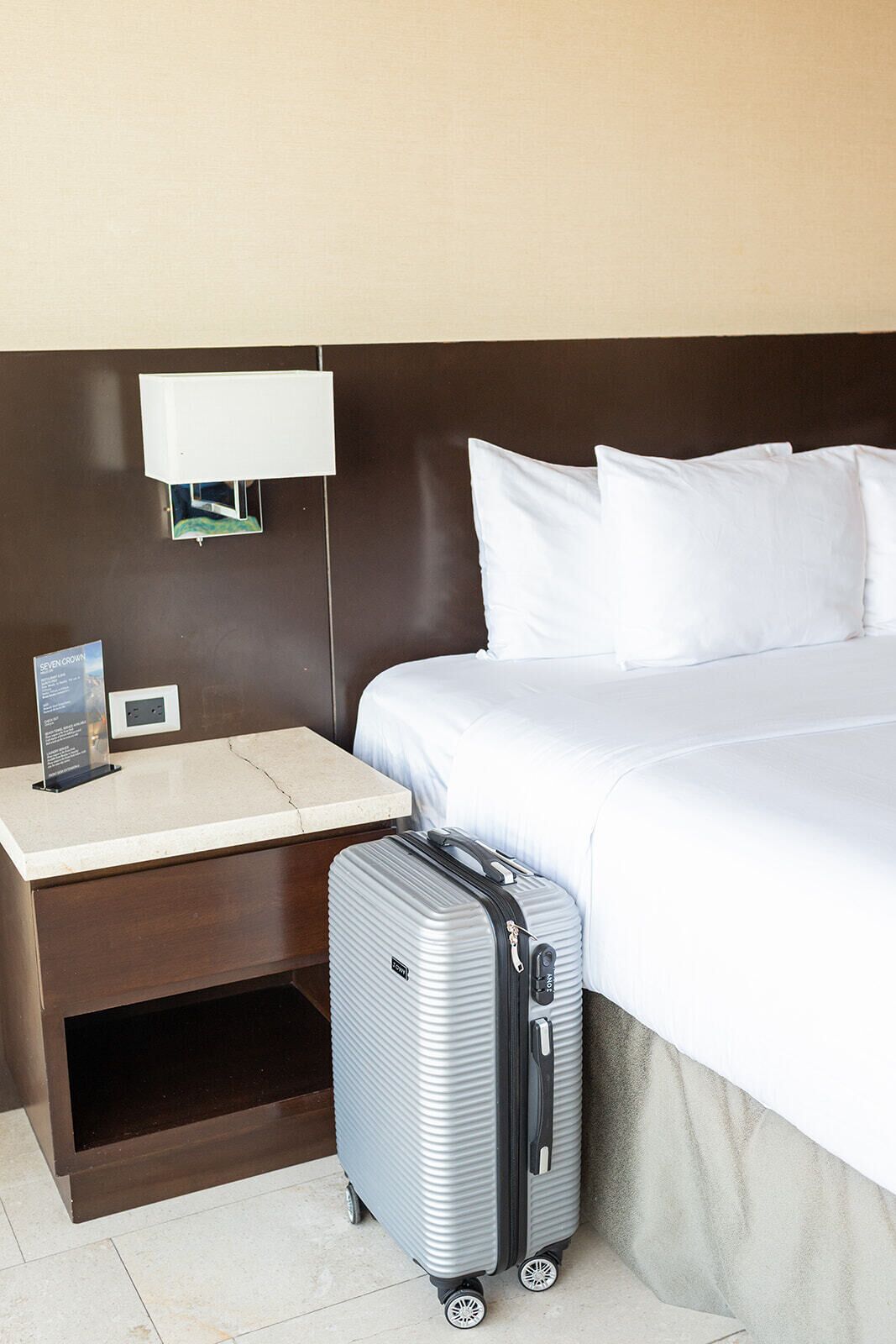 Una habitación de hotel con cama, mesita de noche, lámpara y maleta.