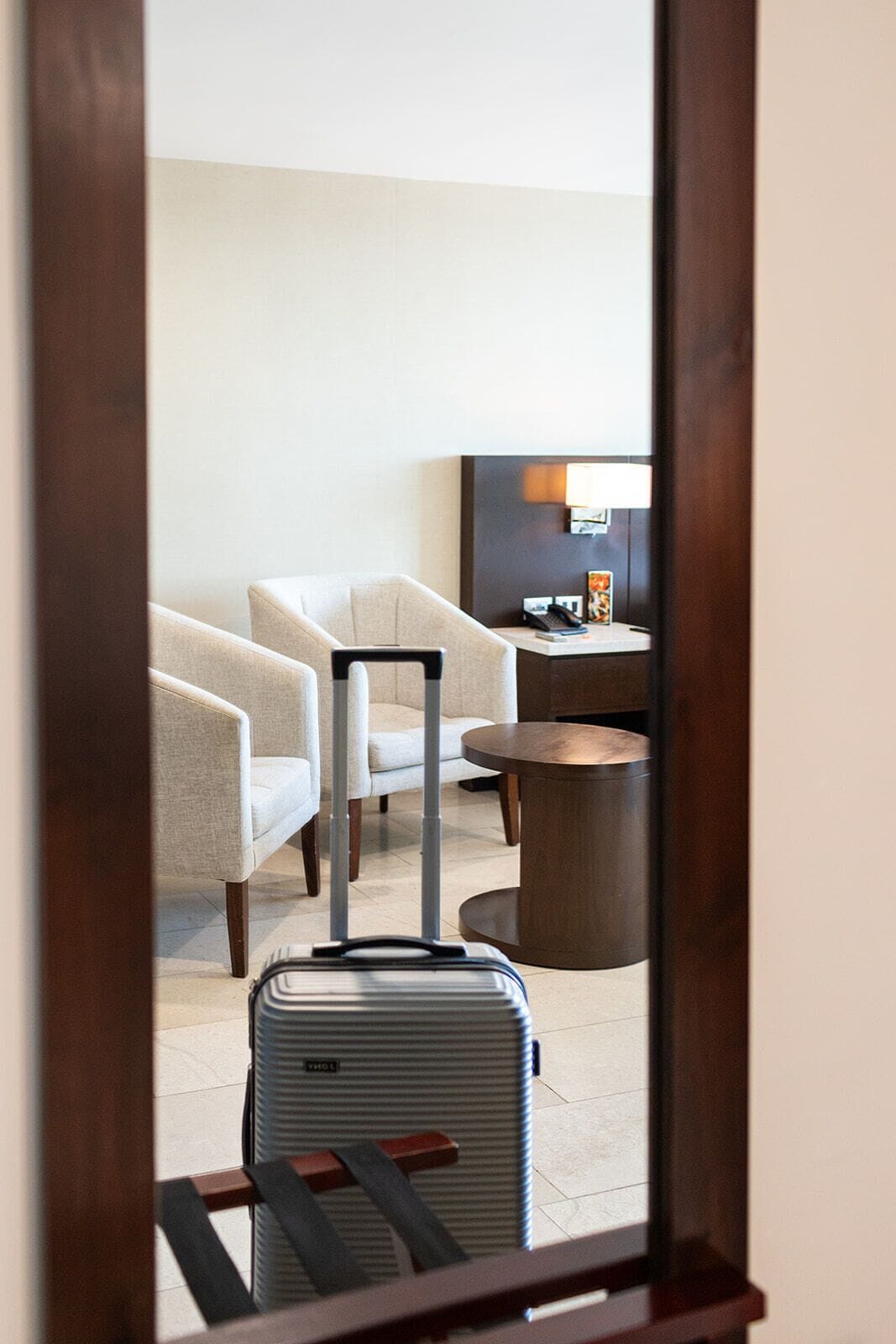 A hotel room with a bed, a chair, a table, and a suitcase.