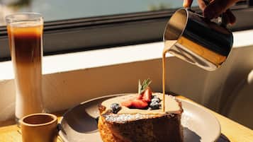 A dessert with fruit on a plate, a glass of a beverage, and a hand pouring a liquid.
