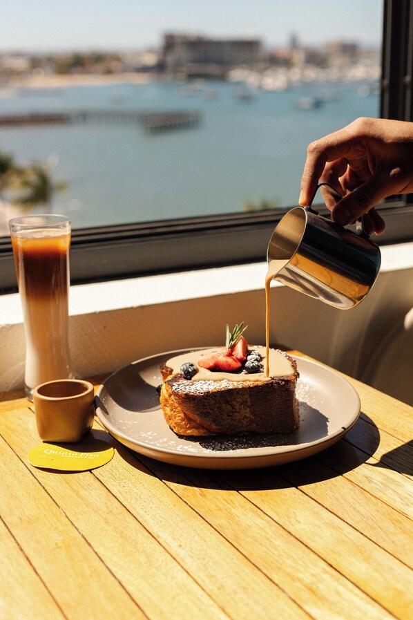 A dessert with fruit on a plate, a glass of a beverage, and a hand pouring a liquid. - Seven Crown La Paz Malecon (La Paz)