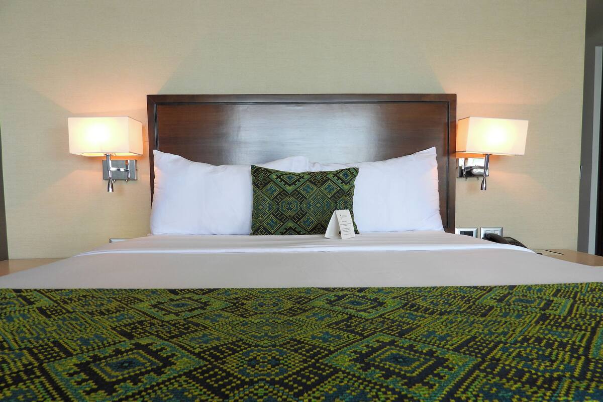 A hotel room with a large bed, two bedside lamps, a headboard, and a patterned bedspread.