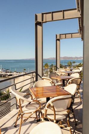 An outdoor seating area with tables and chairs, overlooking a body of water and distant mountains. - Seven Crown La Paz Malecon (La Paz)