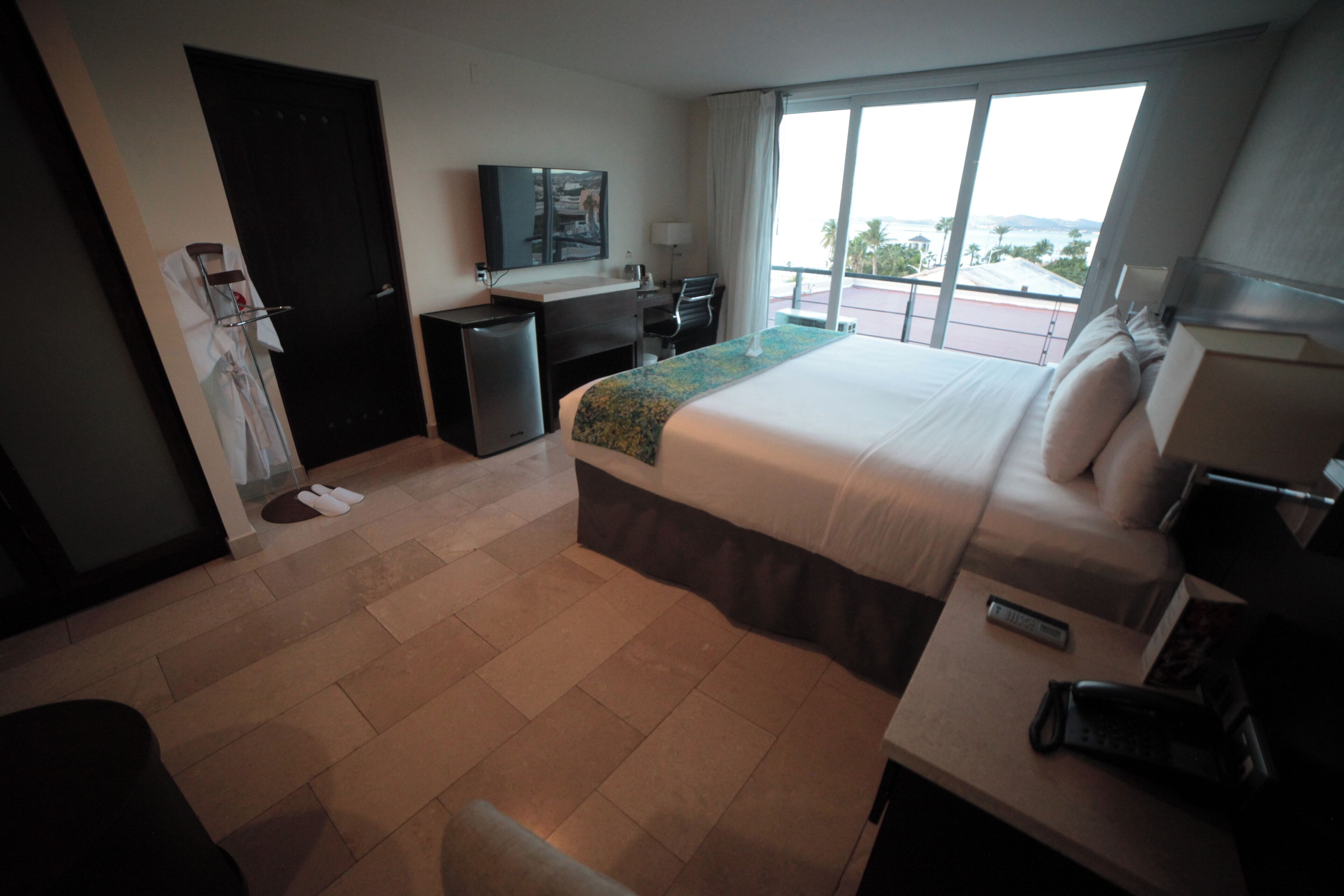 A hotel room with a bed, desk, chair, and a TV on the wall.