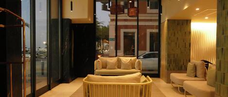 Una habitación de hotel moderna con un ventanal grande, un sofá, una silla y una cesta de mimbre.