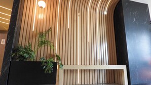 Un interior moderno con un muro curvo de madera, una maceta negra con plantas verdes y un banco blanco.