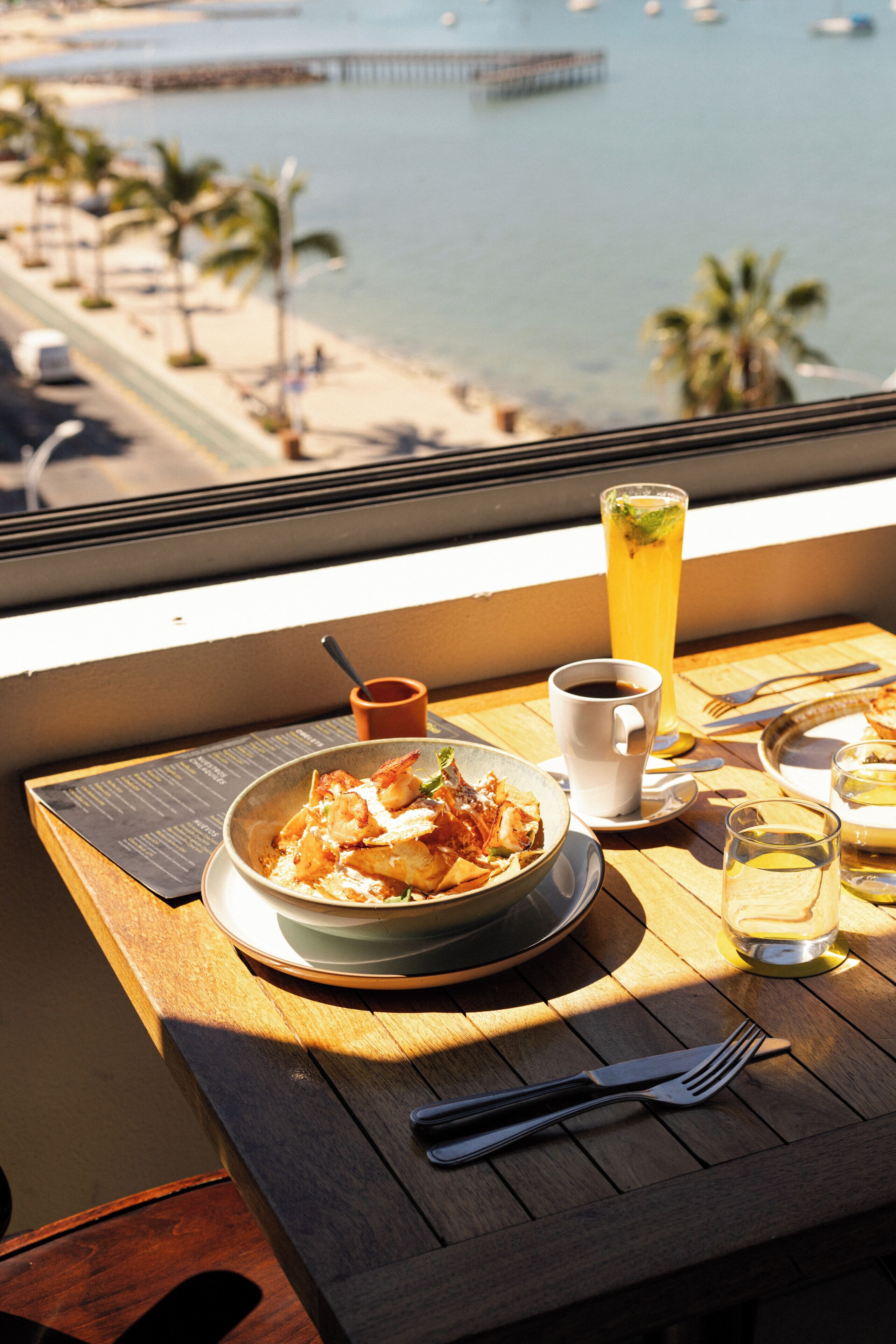 Ett matbord med en måltid, ett glas iste och utsikt över havet och stranden.