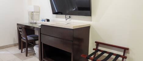 A small, dark wood desk with a flat-screen TV mounted above it, a chair, a small table, and a wooden rack.