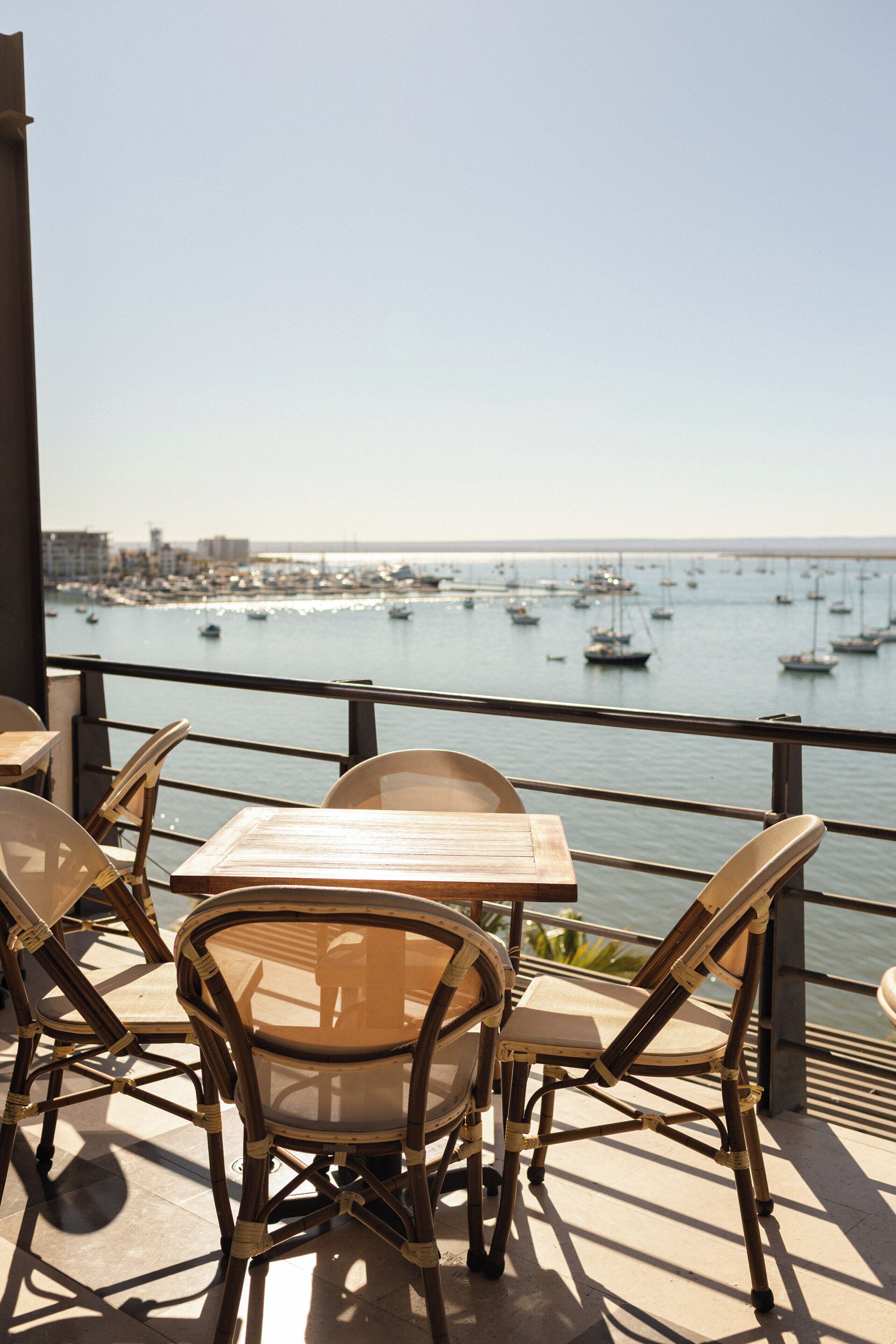 A terrace with tables and chairs overlooking a marina with boats.