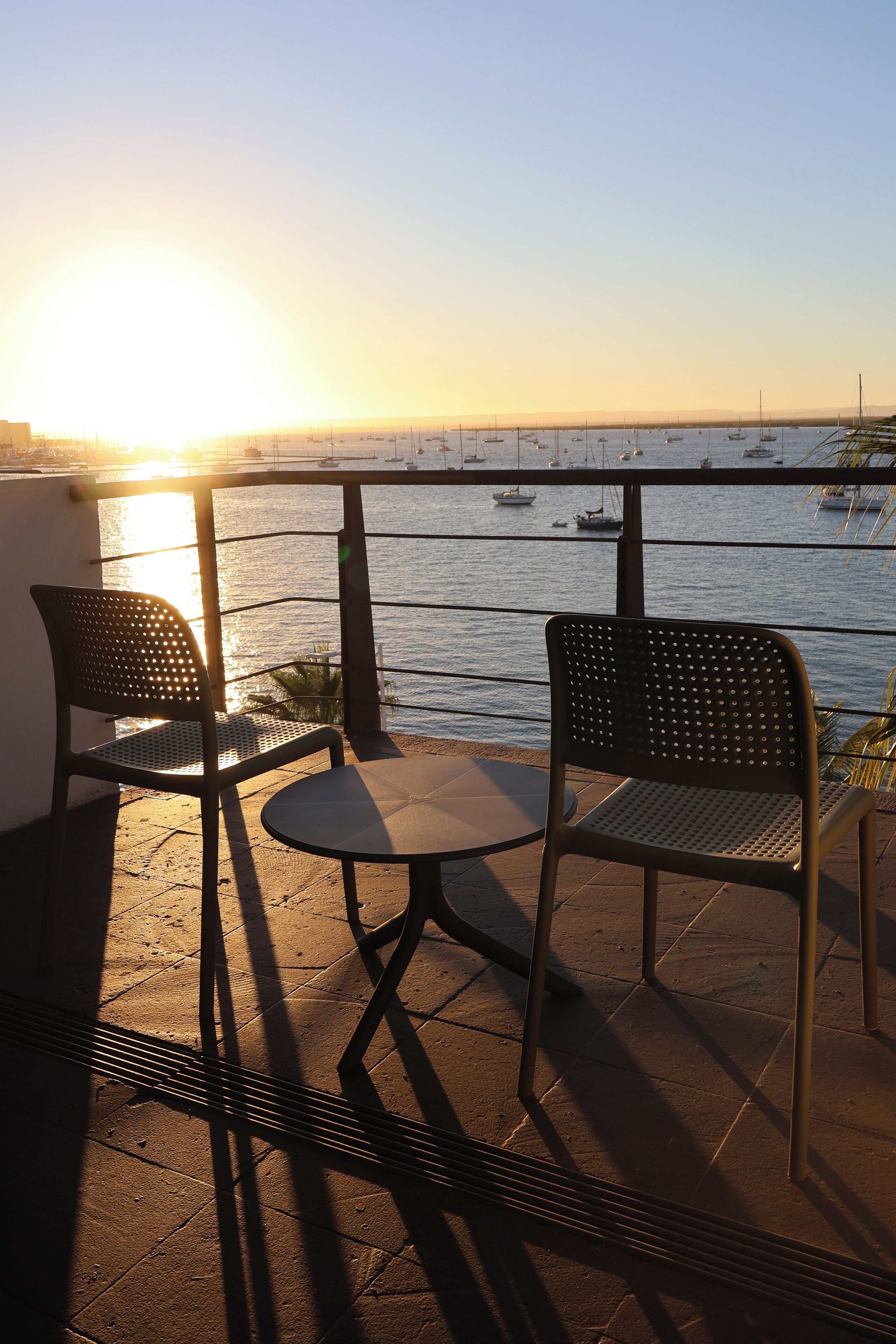 A terrace with two chairs and a table, overlooking a body of water with boats.