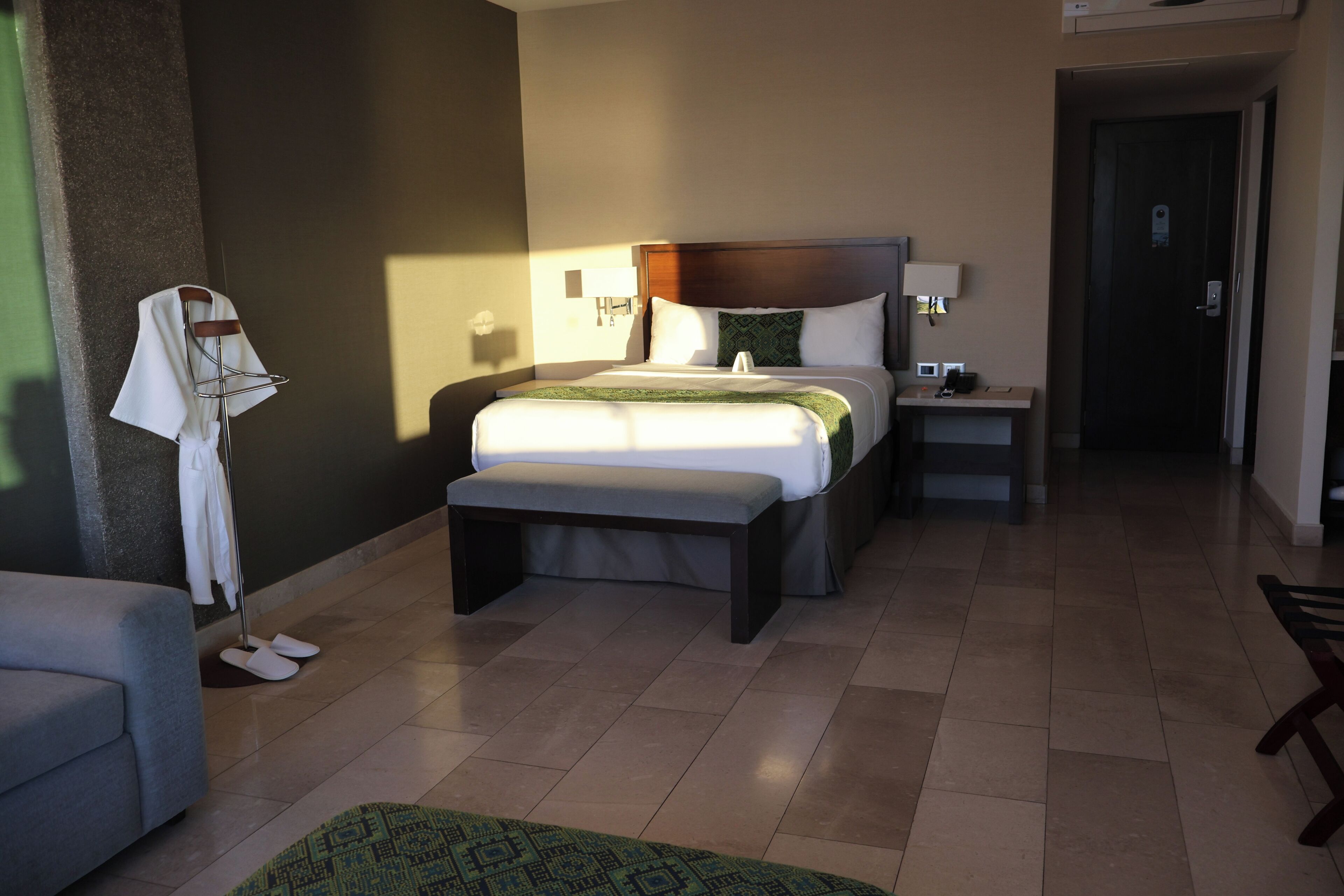 Una habitación de hotel con una cama grande, mesitas de noche, un banco, una pequeña mesa y una silla.