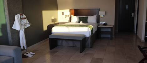 Una habitación de hotel con una cama grande, mesitas de noche, un banco, una pequeña mesa y una silla.