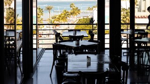 Un restaurante con vistas al océano y a las montañas, con amplios ventanales, mesas y sillas.