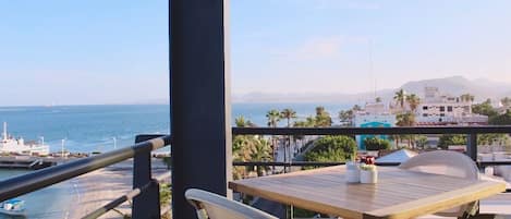 A balcony with a view of the sea, a table with chairs, and a railing.