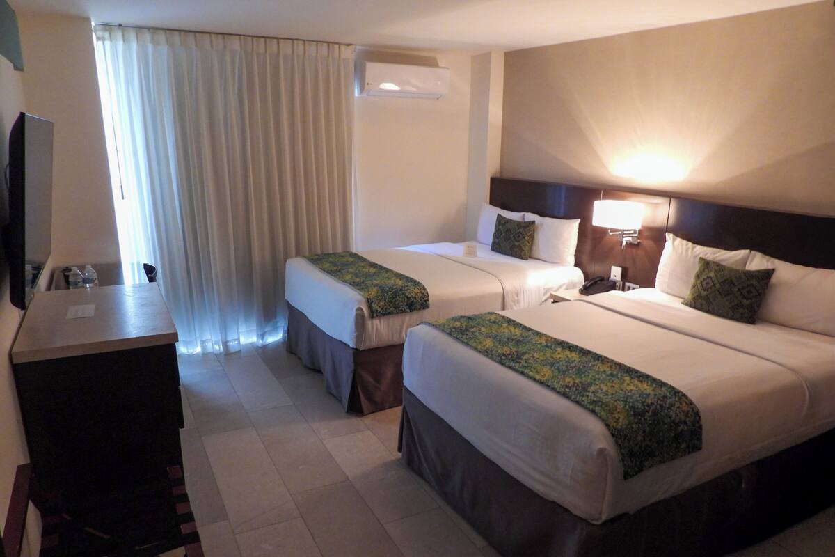 A hotel room with two beds, a desk, and a TV.
