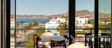 Ein Restaurant mit Außenbereich, großen Fenstern und Blick auf das Meer und die Gebäude.
