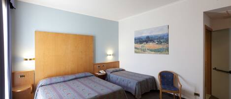 Habitación de hotel con dos camas, cabecero de madera, un cuadro en la pared, una silla y una mesita de noche con un teléfono.