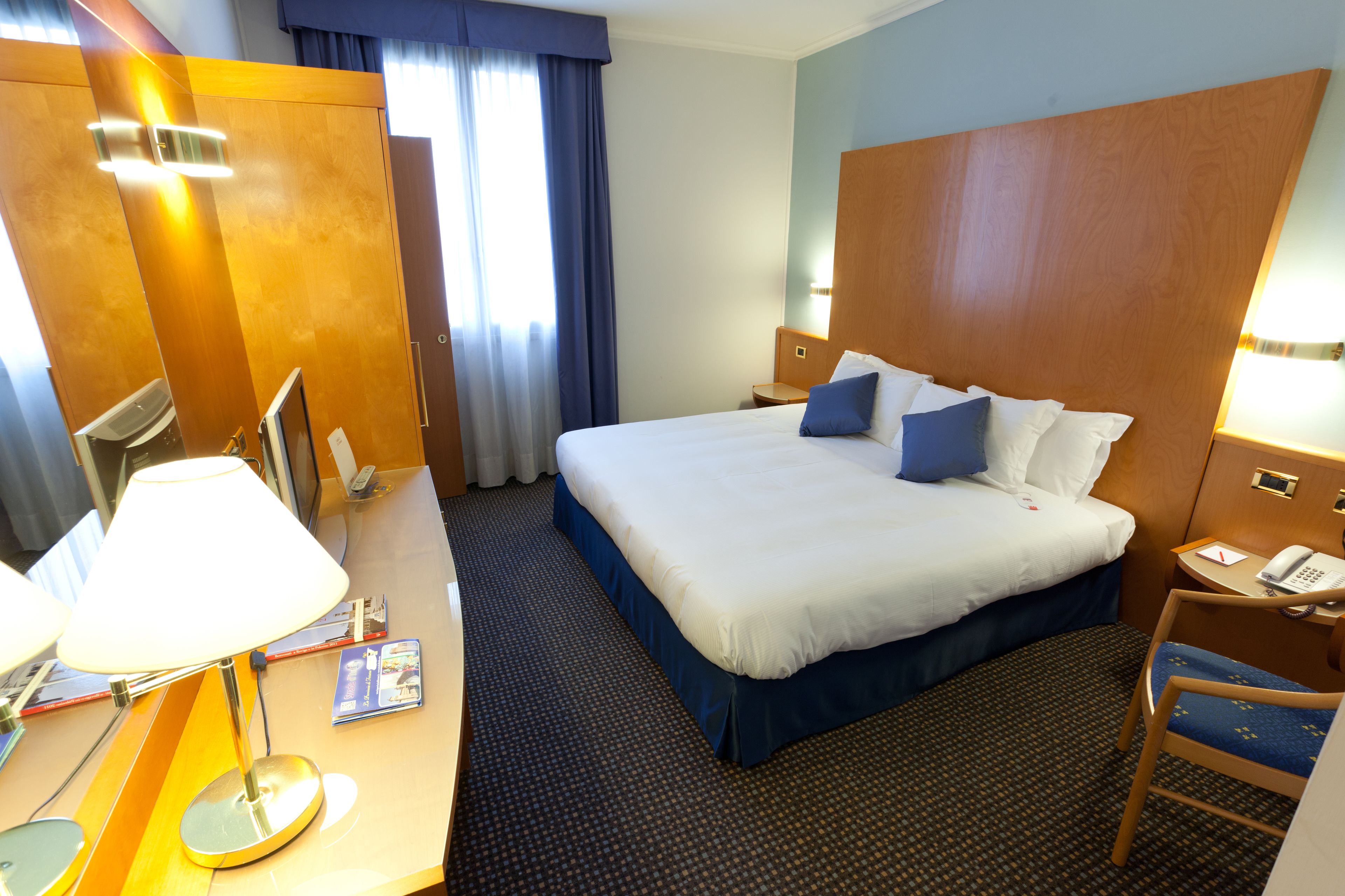 Una habitación de hotel con una cama grande, un escritorio con lámpara, una silla y una mesita de noche con teléfono.
