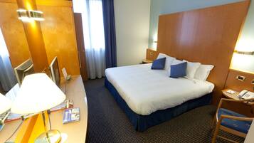 Una habitación de hotel con una cama grande, un escritorio con lámpara, una silla y una mesita de noche con teléfono.