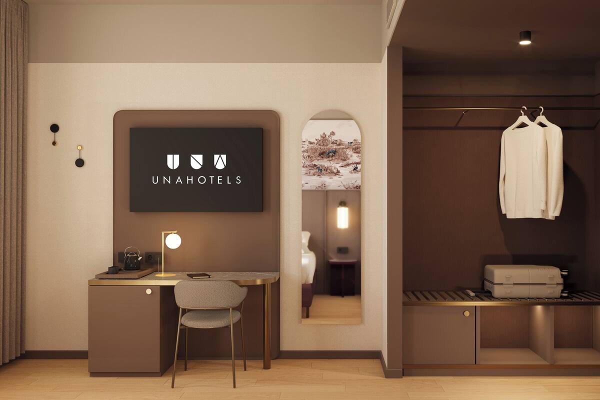 A modern hotel room with a desk, chair, and a coat rack with a white coat.