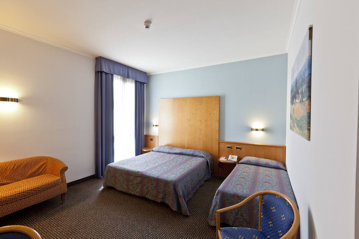 A hotel room with two beds, a sofa, a chair, a nightstand, and a painting on the wall.