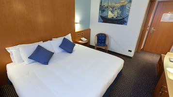 Een hotelkamer met een groot bed, een stoel, een schilderij aan de muur en een deur.