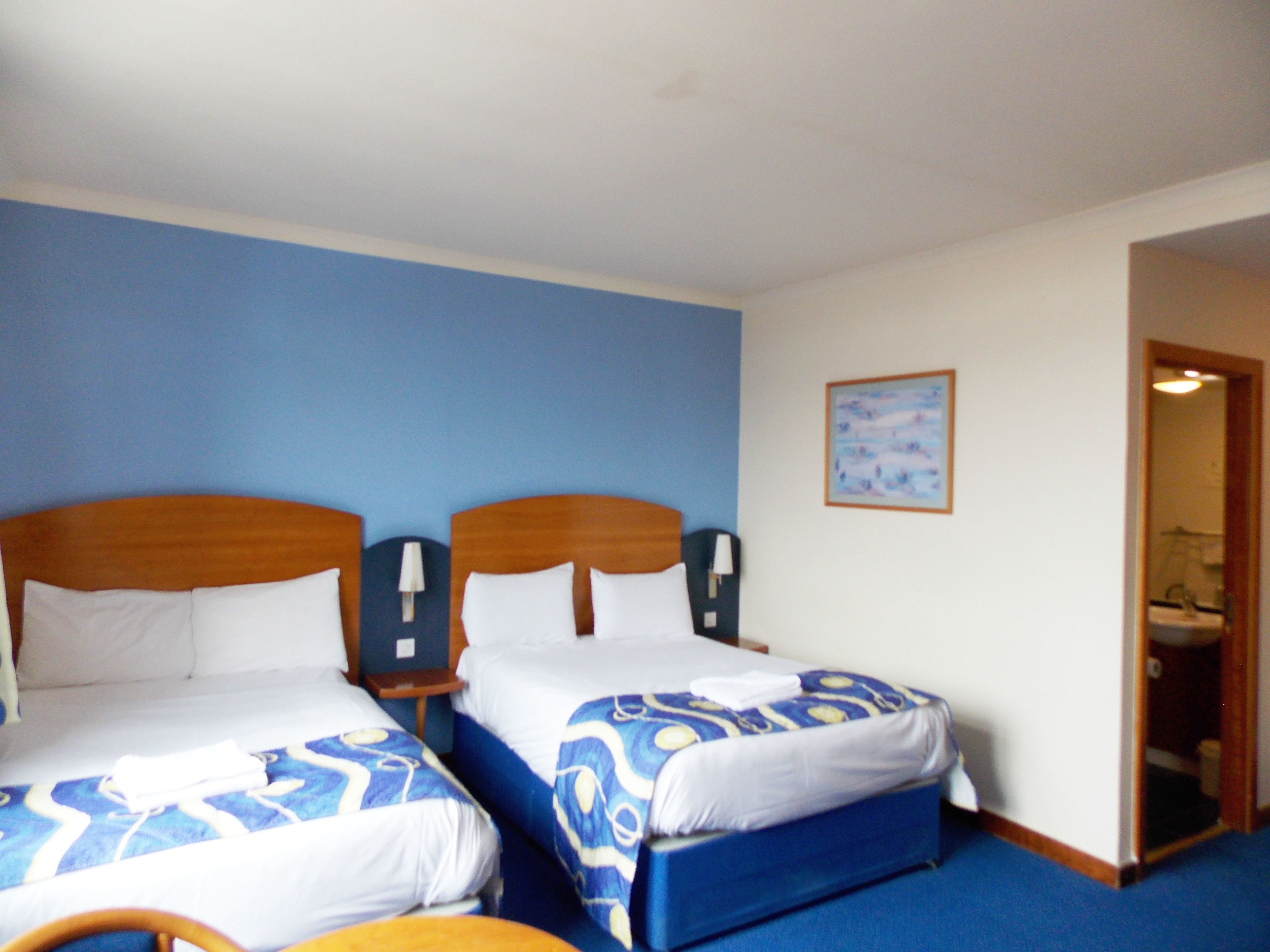 Ein Hotelzimmer mit zwei Betten, jeweils mit einer blau-weißen Bettdecke, einem hölzernen Kopfteil und einem Nachttisch mit Lampe.