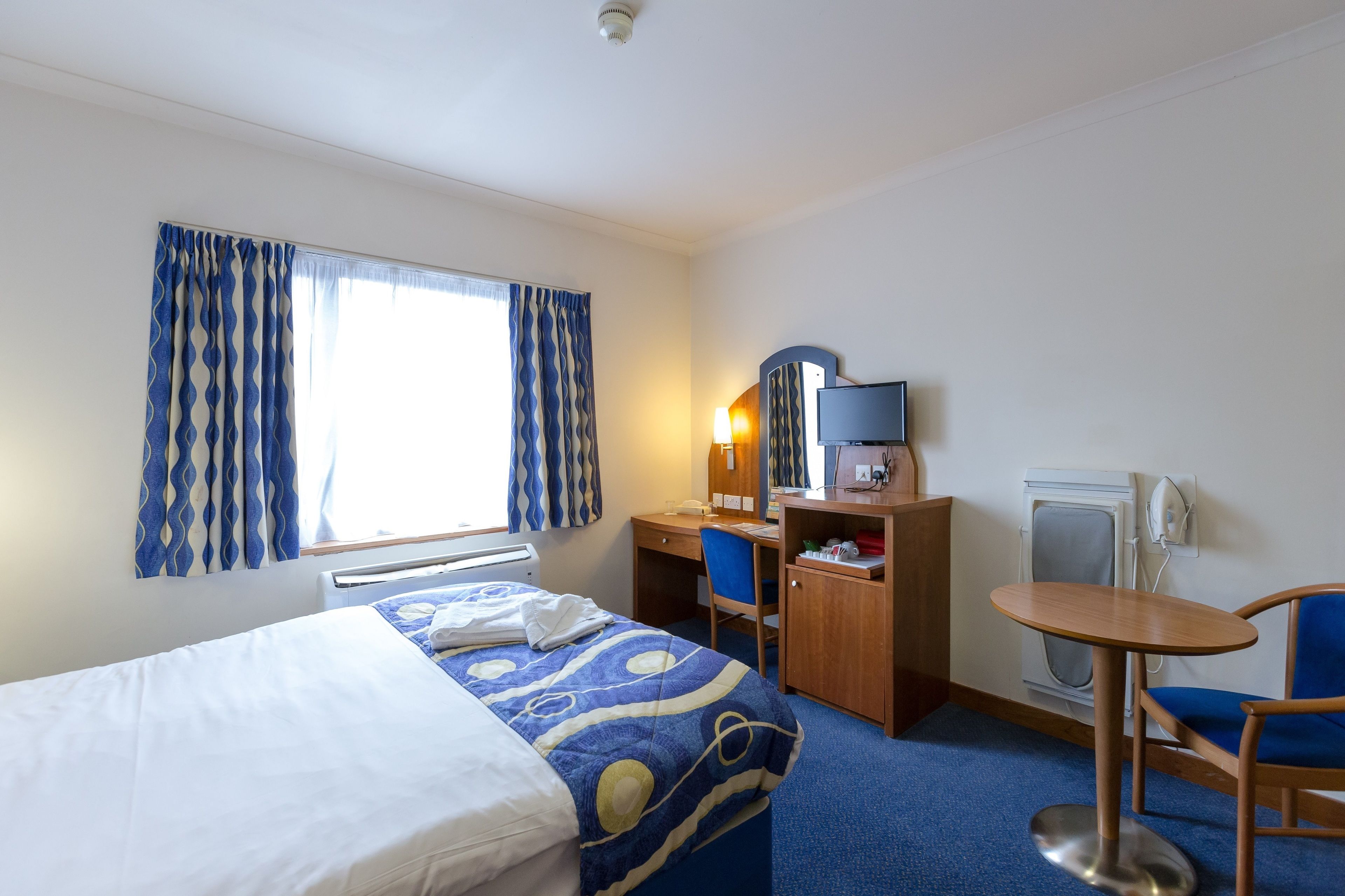 A hotel room with a bed, desk, chair, and a small table.
