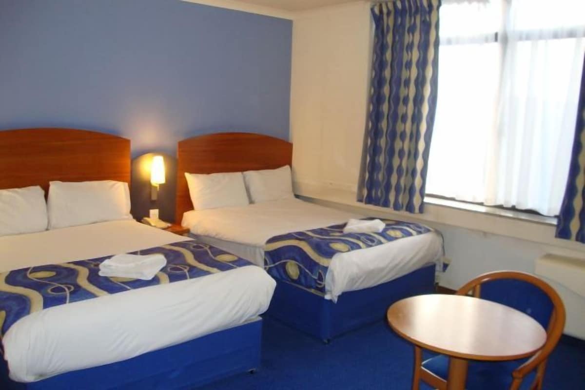 A hotel room with two beds, a small table, and a window with curtains.