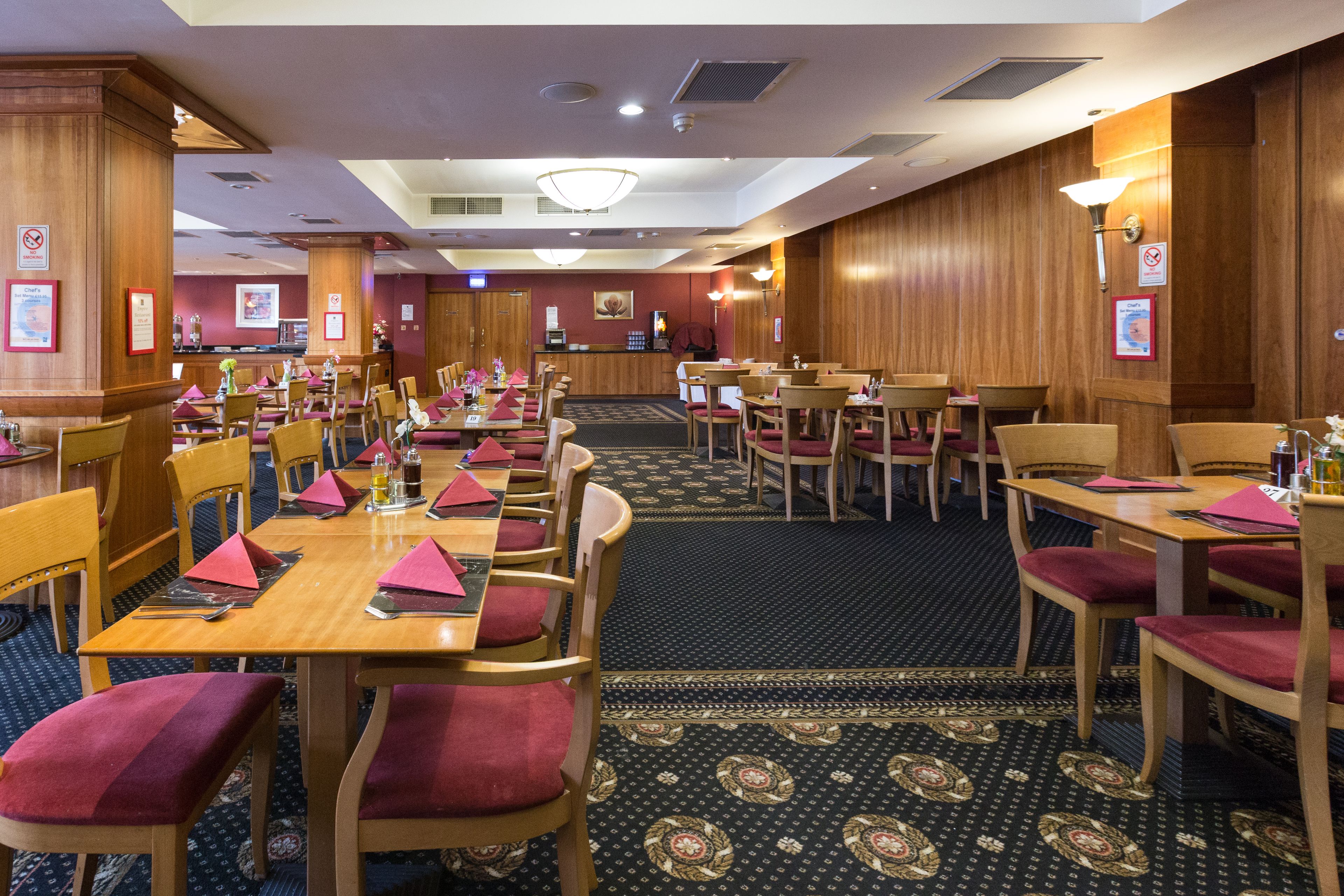 Un comedor de hotel con varias mesas y sillas, una recepción y una alfombra estampada.
