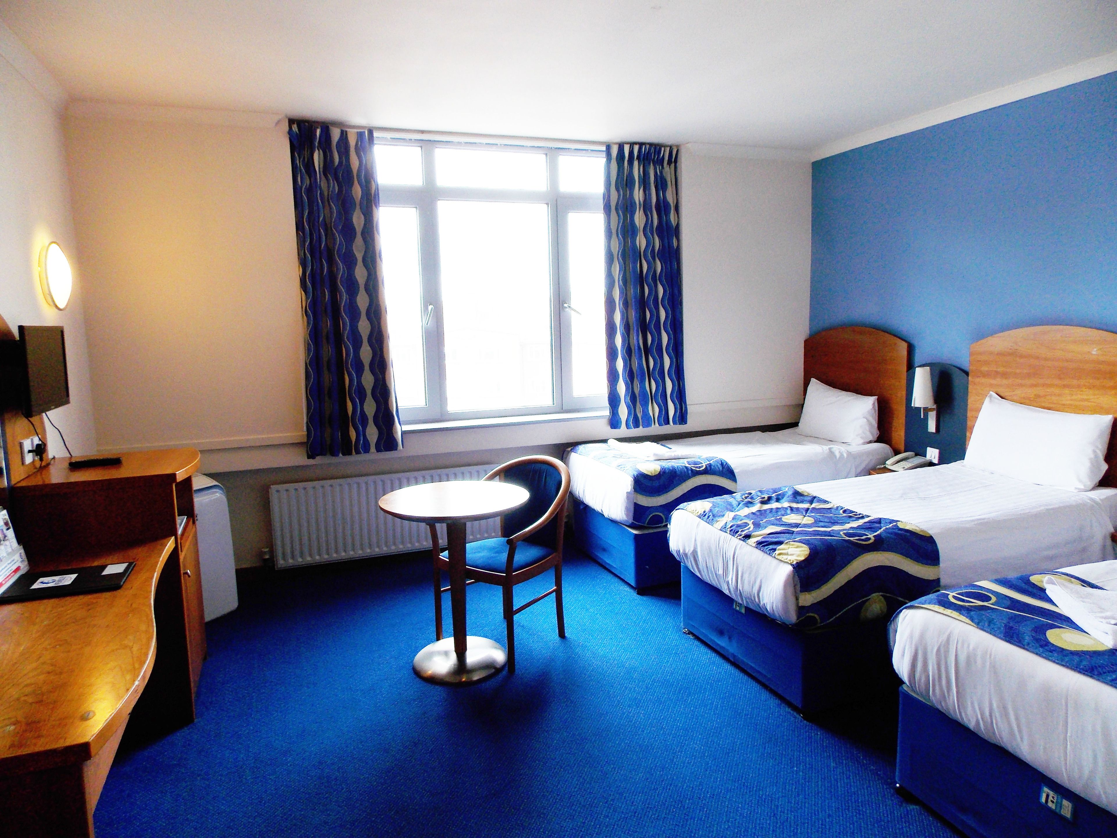 A hotel room with two beds, a desk, a chair, and a small table.