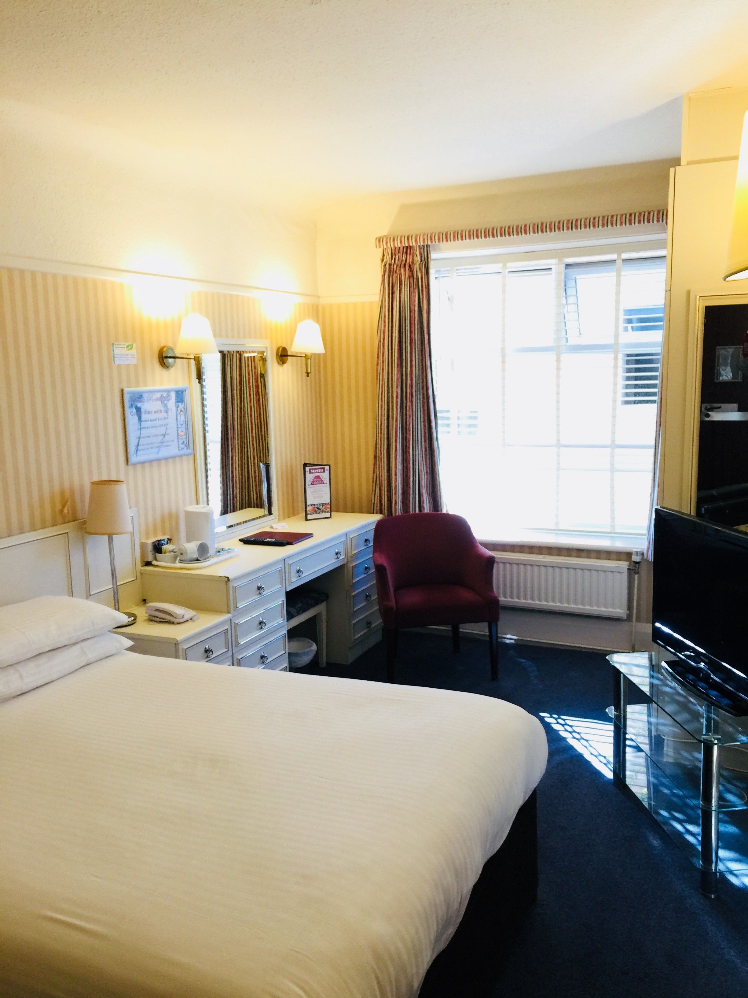 Une chambre d’hôtel avec un grand lit, un bureau avec une chaise, une télévision et une fenêtre avec des rideaux.
