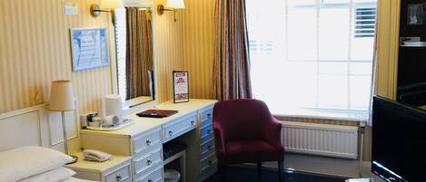 Une chambre d’hôtel avec un grand lit, un bureau avec une chaise, une télévision et une fenêtre avec des rideaux.
