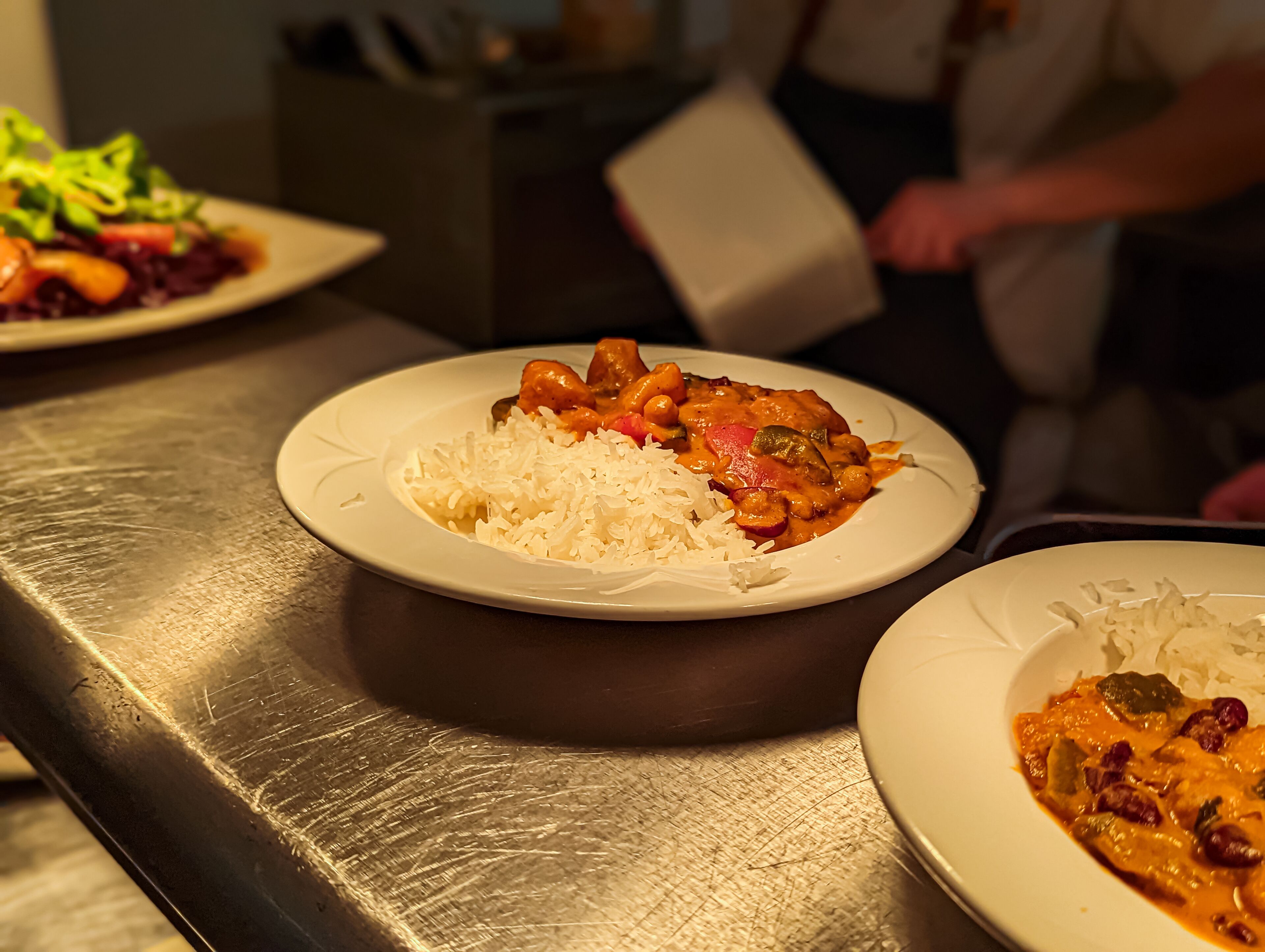 Een roestvrijstalen tafel met borden eten, waaronder rijst en curry.