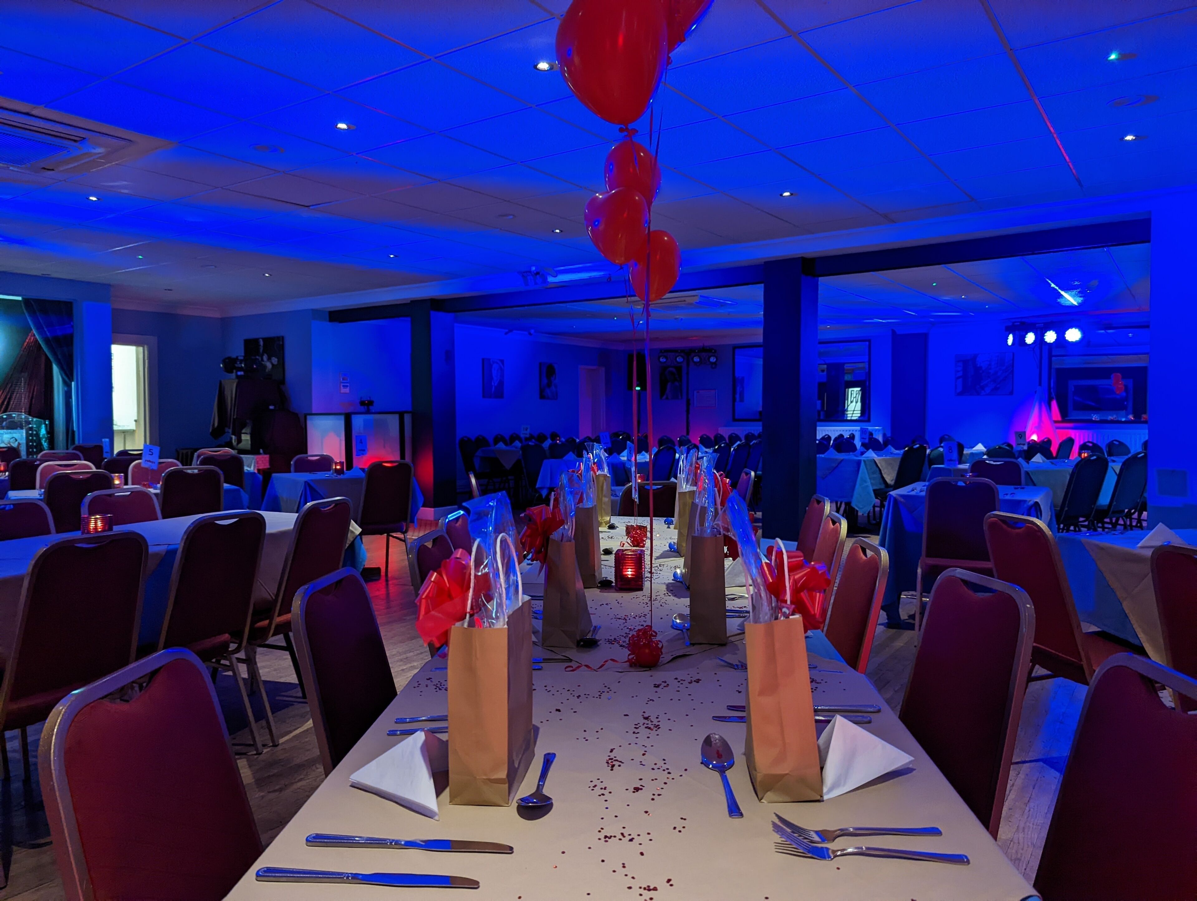 Un salón de banquetes con mesas dispuestas para un evento formal, destacando una larga mesa con mantel blanco, sillas rojas y una decoración central.