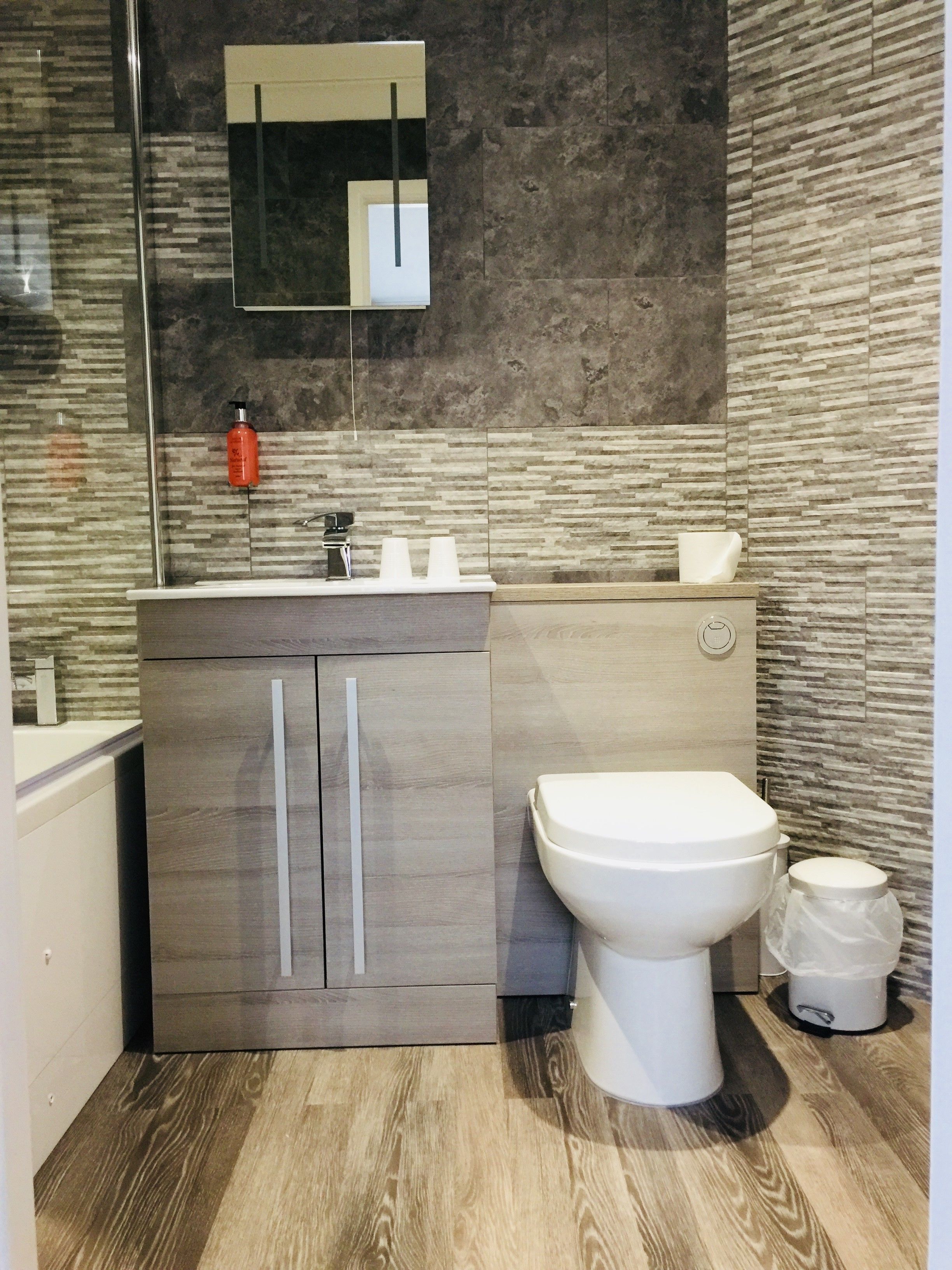 Un baño moderno con tocador de madera, inodoro blanco y espejo sobre el lavabo.