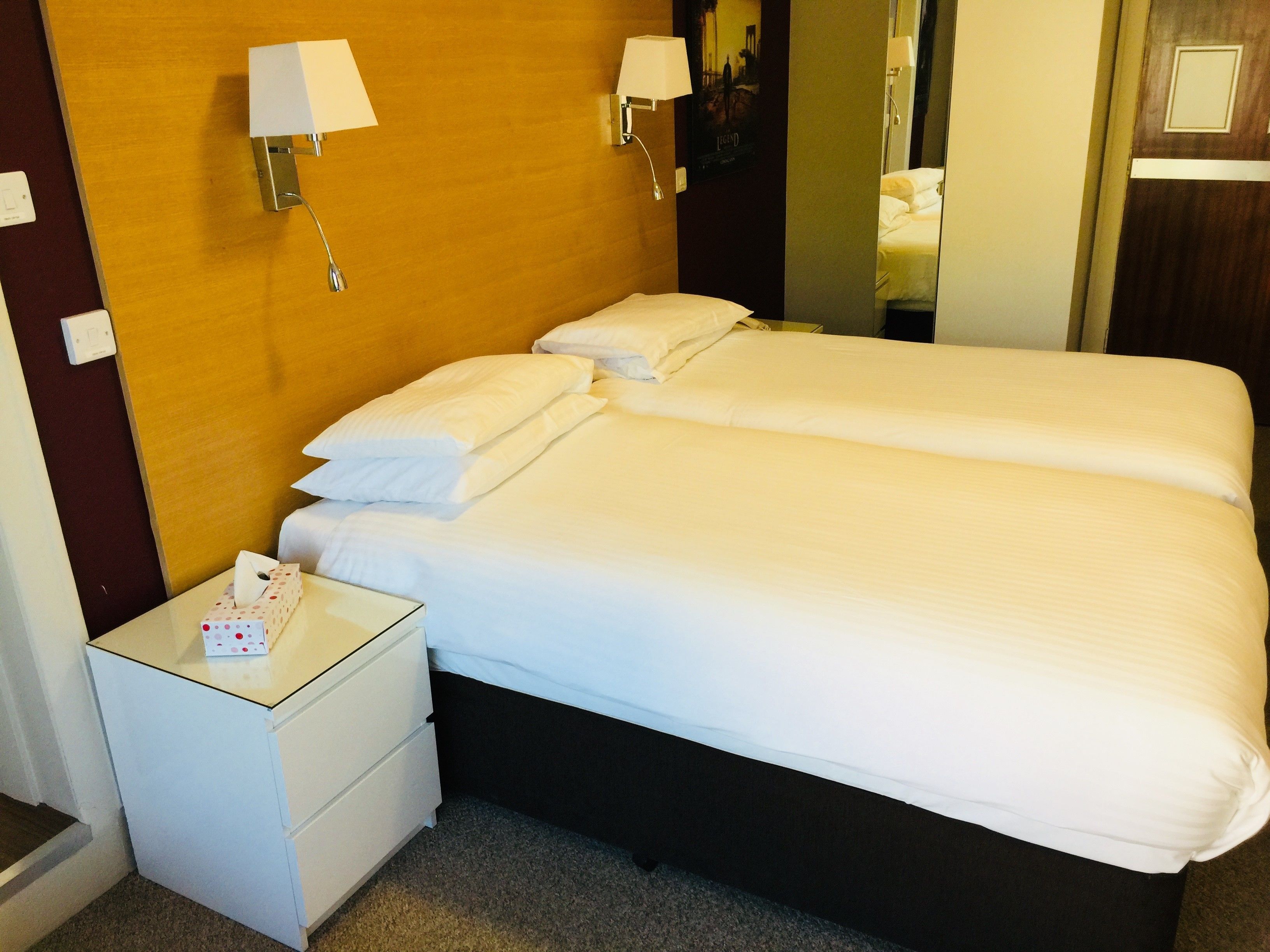 A hotel room with a double bed, two bedside tables, a nightstand, and two wall-mounted lamps.