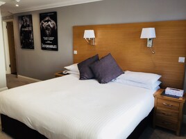 Una habitación de hotel con una cama grande, dos lámparas de noche, un cabecero de madera y dos carteles en la pared.