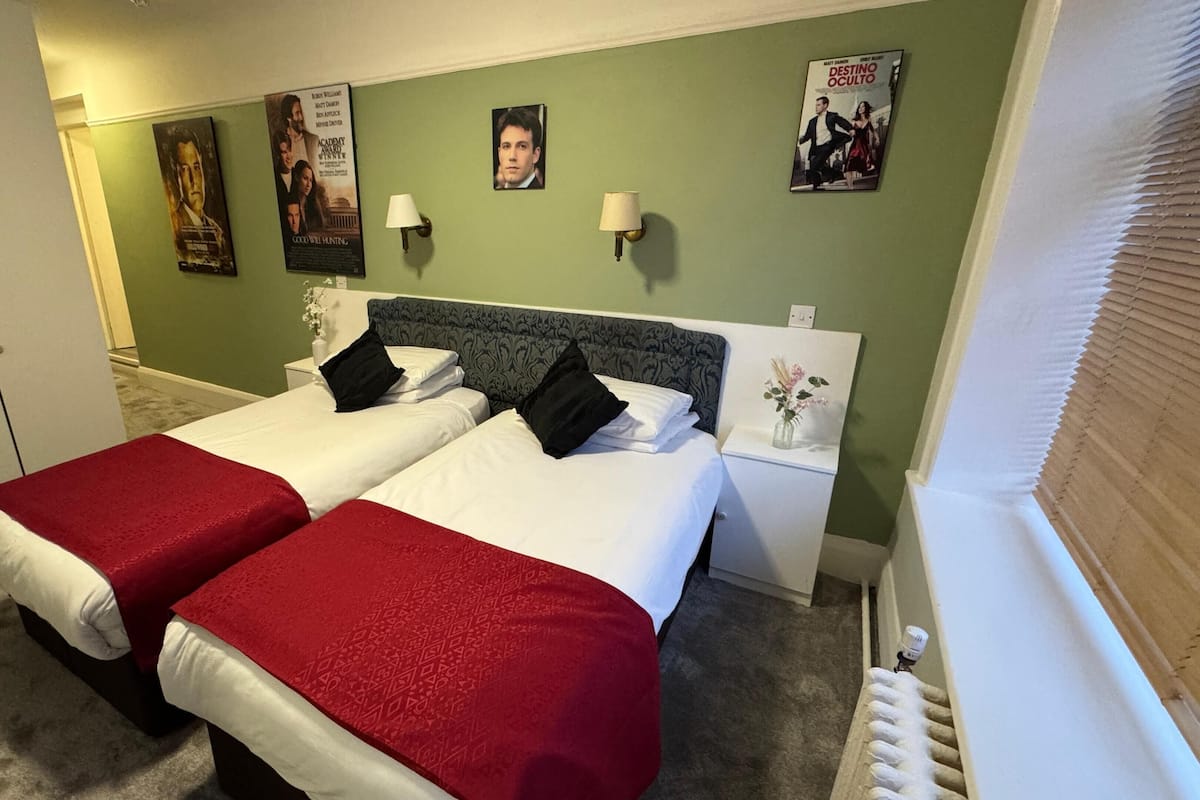 Hotellihuone, jossa on kaksi sänkyä, vihreä seinä, julisteita ja patteri.