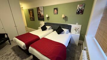 A hotel room with two beds, a green wall, posters, and a radiator.