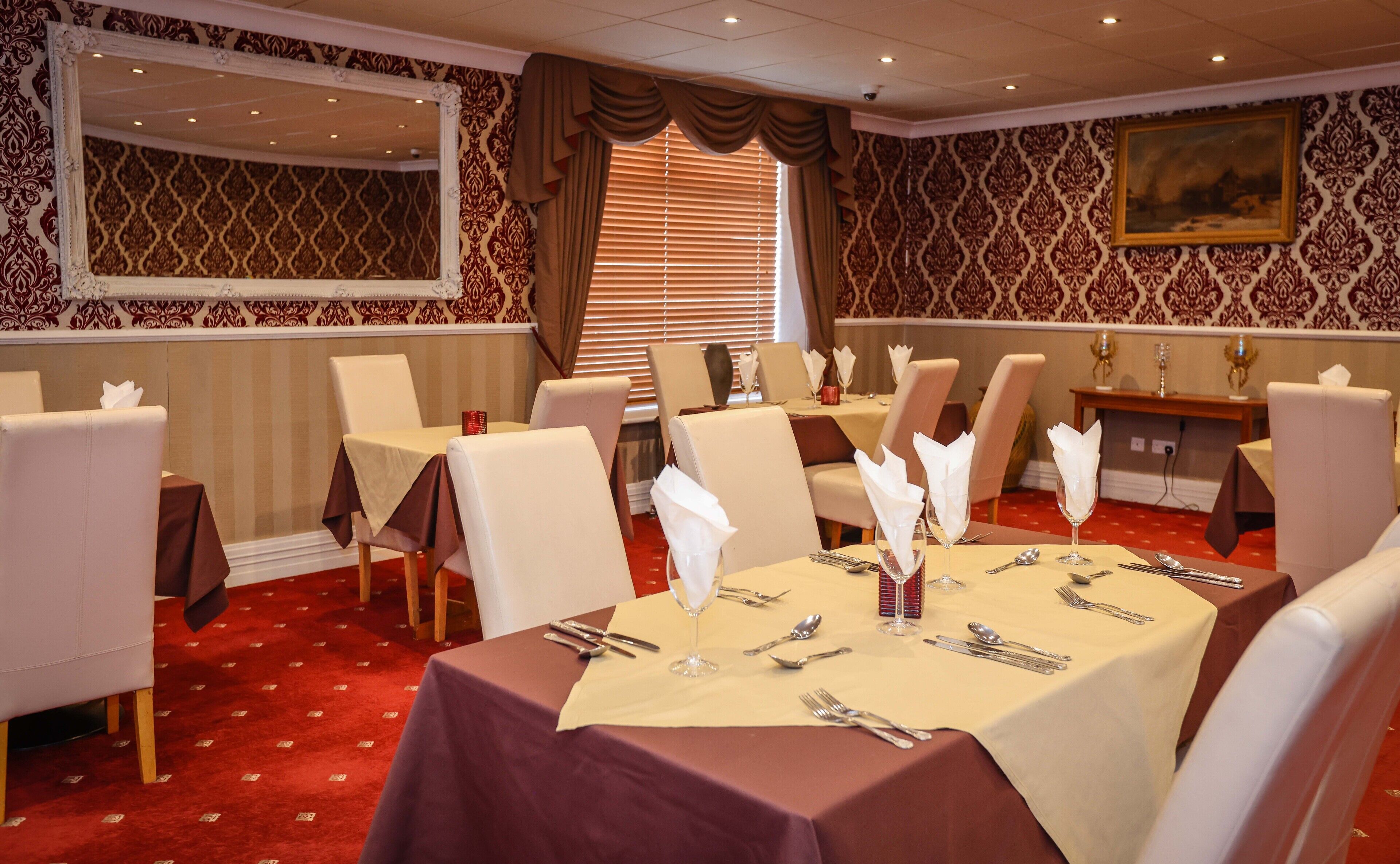 A dining area with tables set for four, chairs, and a large mirror on the wall.